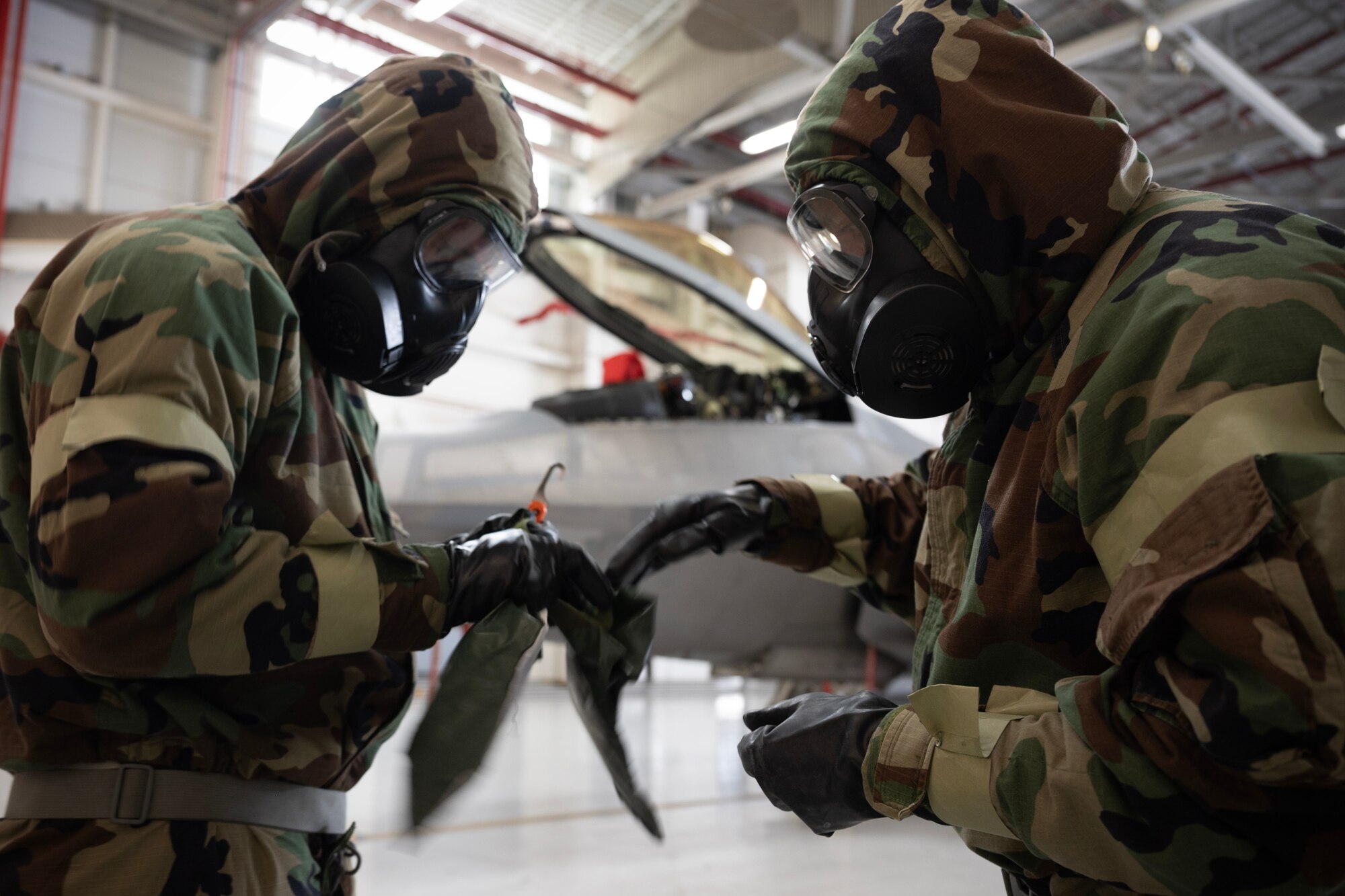 U.S. Air Force Master Sgt. Terrance Akana, 154th Operations Support Squadron aircrew flight equipment craftsman, utilizes an over-cloak that provides an extra layer of protection on Capt. Alex “Doom” Moss, 19th Fighter Squadron F-22 Raptor pilot, during a Next Generation Aircrew Protection Step-Launch and Recover concept of operation demonstration, Joint-Base Pearl Harbor-Hickam, Hawaii, May 11, 2023. The demonstration showcases the Pacific Air Forces stop gap for the F-22 Aircrew Chemical, Biological, Radiological and Nuclear limiting factor utilizing the modified M-50 ground crew mask. (U.S. Air National Guard photo by Master Sgt. Mysti Bicoy)