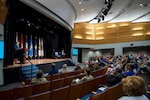 A woman speaks from a stage in an auditorium.