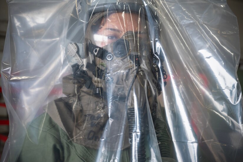 An airman wears an over-cloak over an helmet and mask.