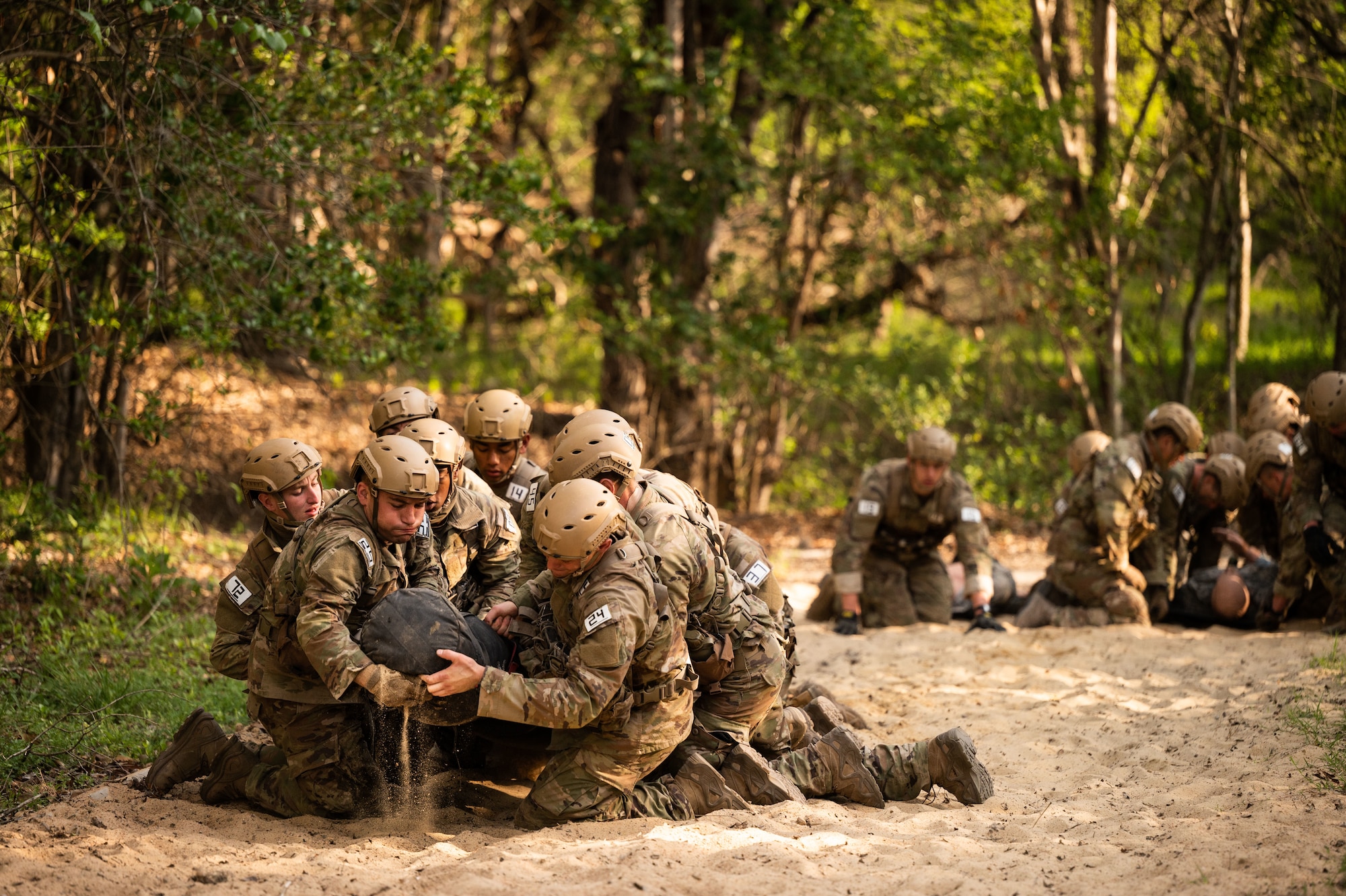 Airmen in full gear and helmets lift heavy log up a sandy hill as a team