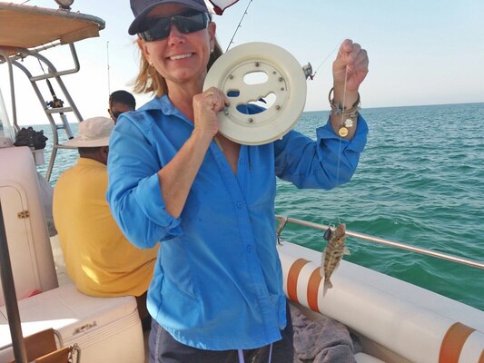 A woman on a boat holds up a fish