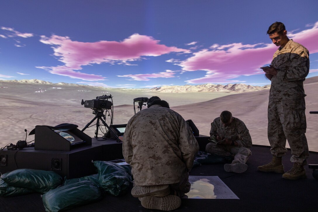 A group of Marines sit and stand on a black tarp with many small devices.