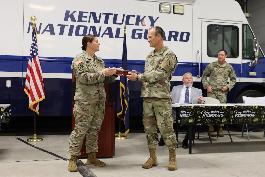 Chief Warrant Officer 4 Jennifer Ritchie, Recruiting and Retention Battalion officer strength manager, presents a retirement gift to Chief Warrant Officer 5 David Barker, Joint Forces Headquarters, Kentucky National Guard, during his retirement ceremony in Frankfort, Ky, April 27, 2023. Barker is retiring after 39 years of service. (U.S. Army National Guard photo by Lt. Col. Carla Raisler Kentucky National Guard)