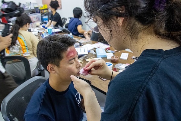 USNMRTC Yokosuka staff apply moulage to an exercise participant for large-scale, multi-day, joint-partner exercise to promote interoperability and readiness