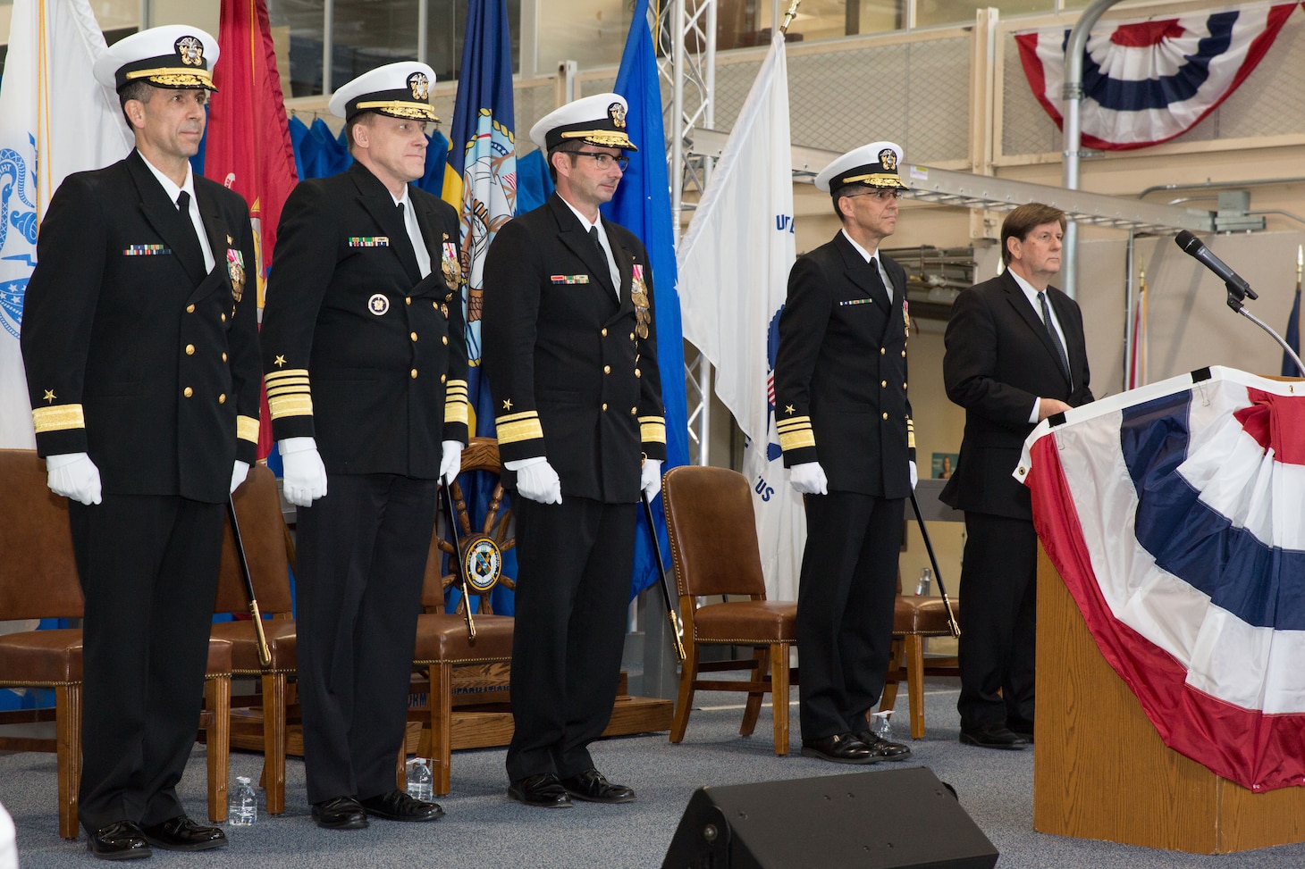 Group of full dressed officers line up on stage behind a podium to prepare for a change of command