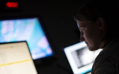 Image of woman intelligence military member looking at multiple computer screens.