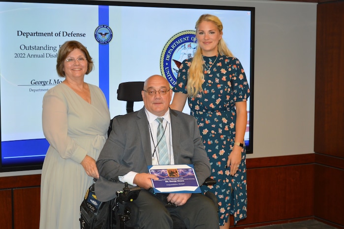 Mr. George Moore (right), program analyst at Strategic Systems Programs received the Secretary of Defense 2022 Outstanding Civilian with a Disability Award Monday, with his wife Mrs. Donna Moore (left) and daughter Kelly (right) by his side. The award honors the accomplishments of individuals who have made significant contributions to their command’s mission and have, at the same time, consistently demonstrated the core values of their command. (Photo by Joseph Ross/Released)