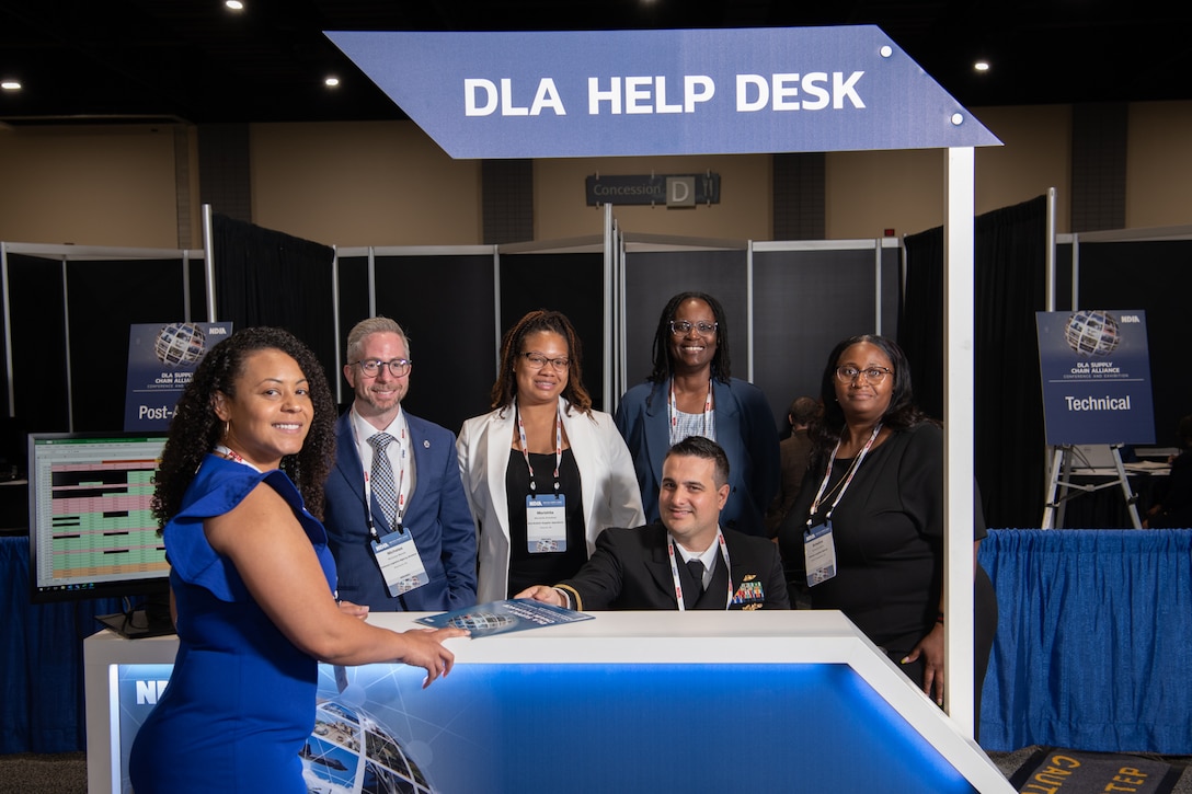 A group of people pose at a help desk on a conference floor.