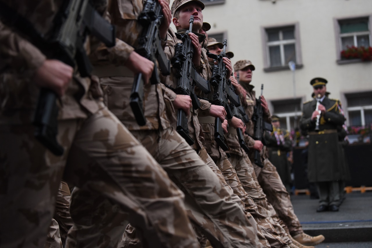 Soldiers march in formation carrying rifles.