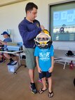 Navy Diver 2nd Class Cameron Duffy, Pearl Harbor Naval Shipyard and Intermediate Maintenance Facility (PHNSY&IMF), left, places a KM 37 hard hat helmet (diving helmet) on a child’s head at the PHNSY & IMF demonstration table during the Onizuka Day of Exploration.