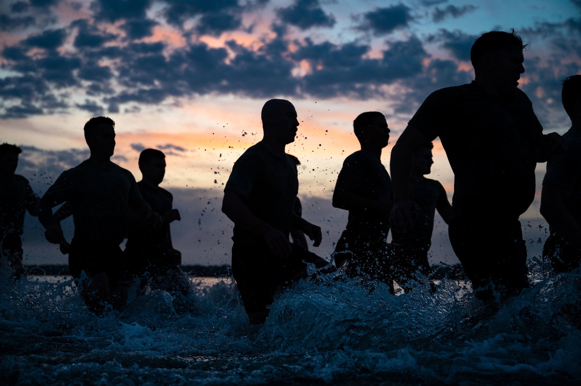 silhouettes run through the shallow ocean, splashing water as the sun rises colorfully behind them