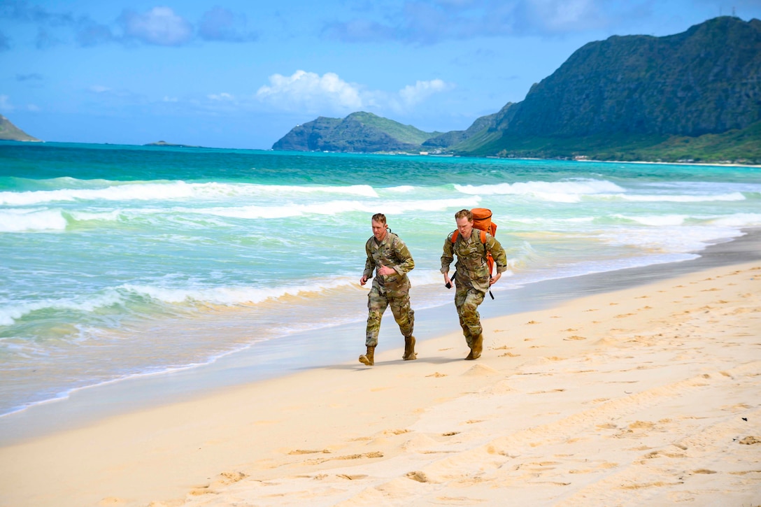 Two soldiers run on a beach.