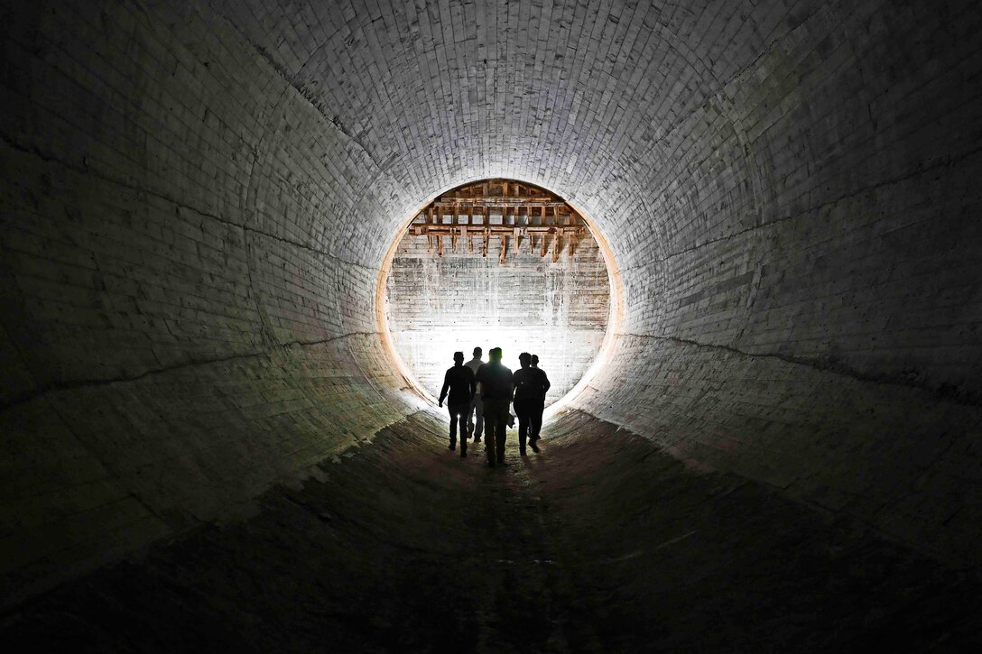 People shown in silhouette walk through a tunnel.