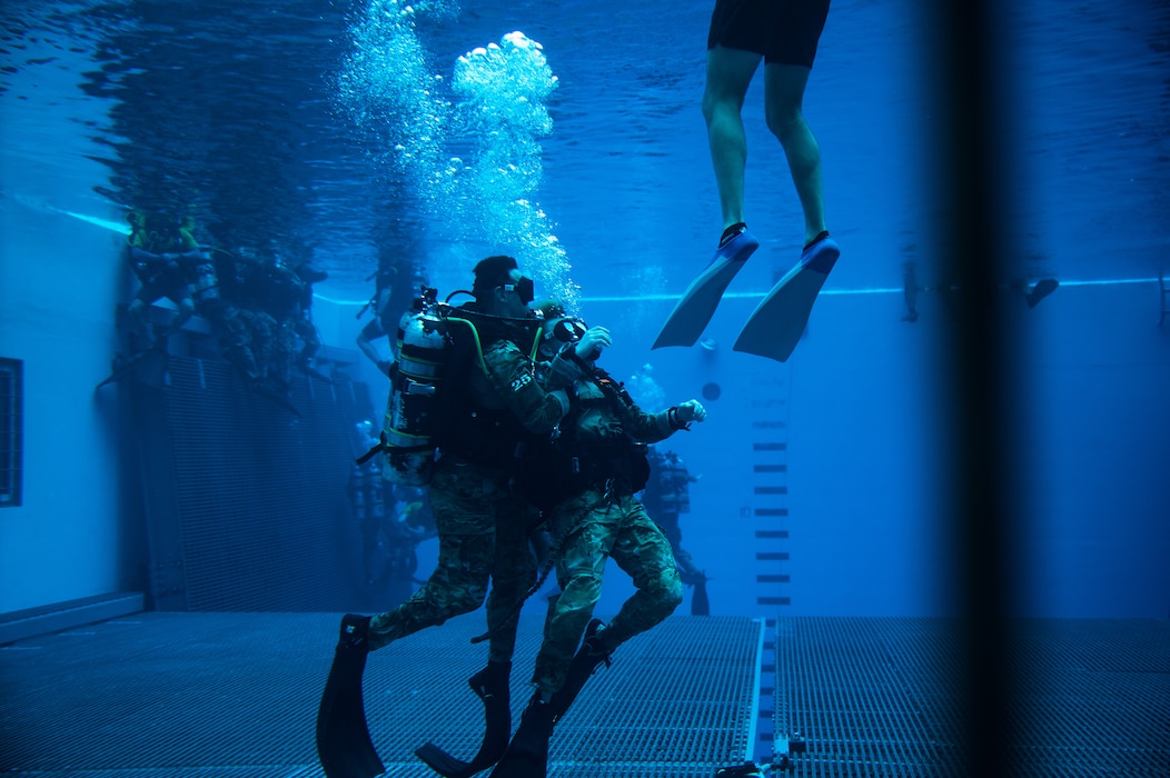 under water, students in scuba gear begin to rise to the surface, bubbles all around