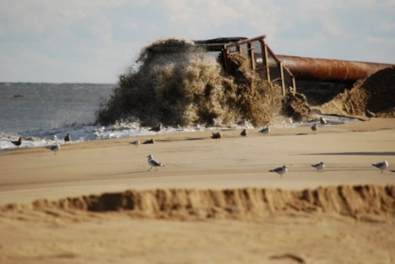 Sand and water pours through a pipe and basket onto the beach