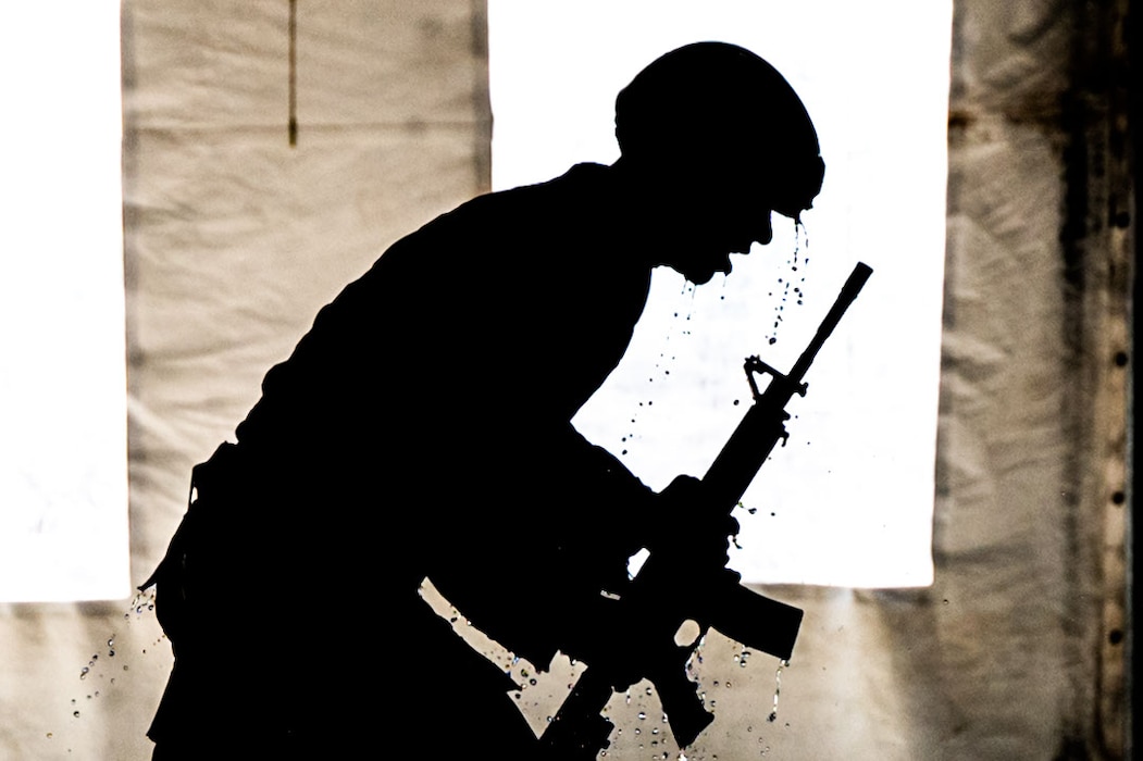 silhouette of airman in full gear with training gun as he emerges from the pool, dripping wet