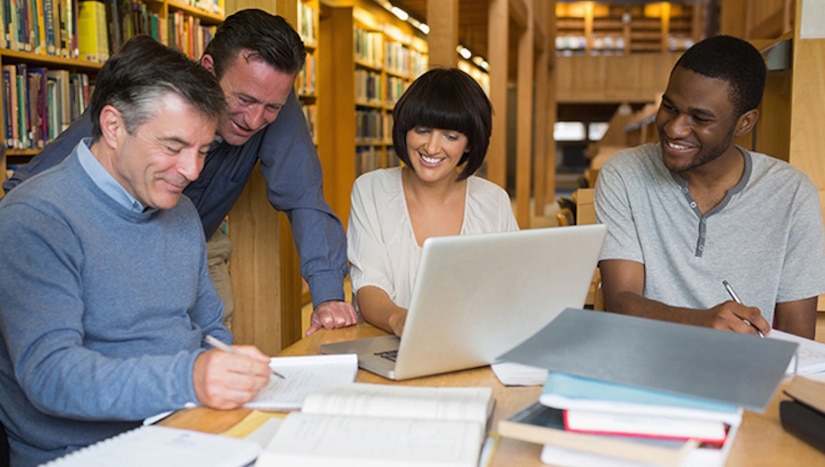 A group of people sit around a computer.