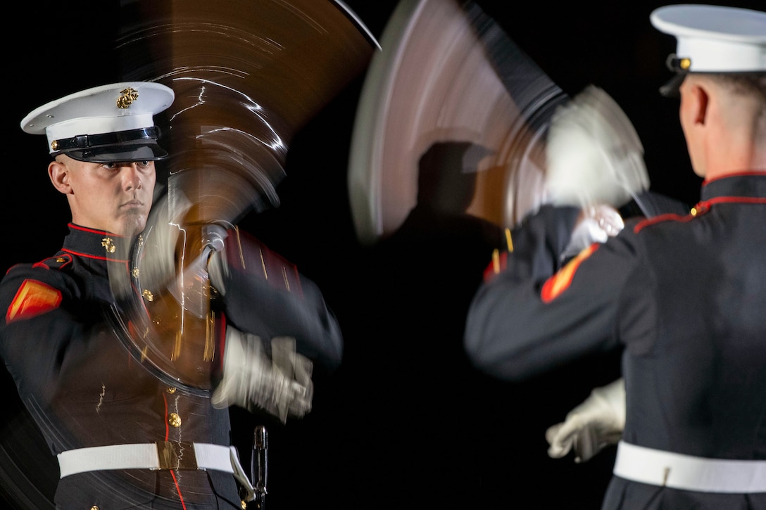 Two Marines face each other while rotating rifles in the dark.