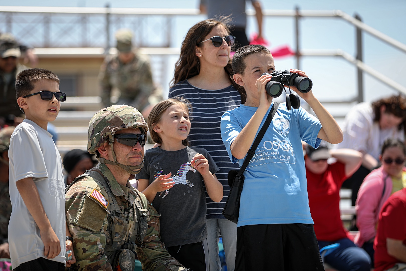 2nd Lt. Michael Elizondo, an officer assigned to the 1st Battalion, 160th Field Artillery, 45th Infantry Brigade Combat Team, kneels with his family as they look onto a firing line of three artillery batteries at a family day live-fire demonstration hosted by the battalion on May 20, 203 at Fort Sill, Oklahoma. The event was the second annual Family day live-fire event that the battalion hosted as a way to strengthen the bonds between Soldiers and their families, as well as the overall community. (Oklahoma National Guard photo by Pfc. Anthony Ackah-Mensah)