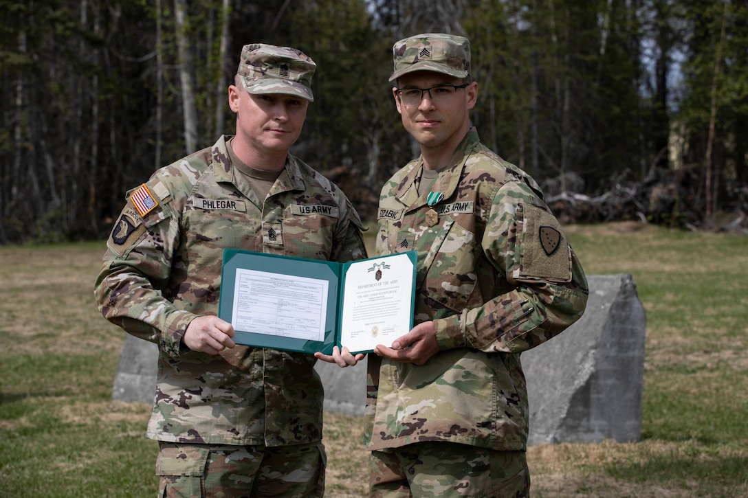 Command Sgt. Maj. John Phlegar, left, the state command sergeant major of the Alaska Army National Guard, presents the Army Commendation Medal on the 2023 Non-Commissioned Officer of the Year, Sgt. Robert Dzabic, a CH-47 Chinook helicopter repairer, during the Best Warrior Competition awards ceremony held at Camp Carroll, Alaska, May 21, 2023. Throughout the week of May 16, 2023, the Best Warrior Competition tested Soldiers on their physical and mental readiness as well as their knowledge of Army doctrine and common warrior tasks.
