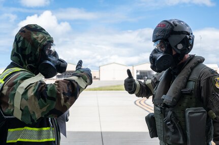 Two Airmen wearing CBRN protective gear give each other the thumbs up