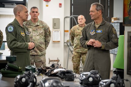 Two U.S. Air Force leaders stand talking with CBRN mask gear in front of them