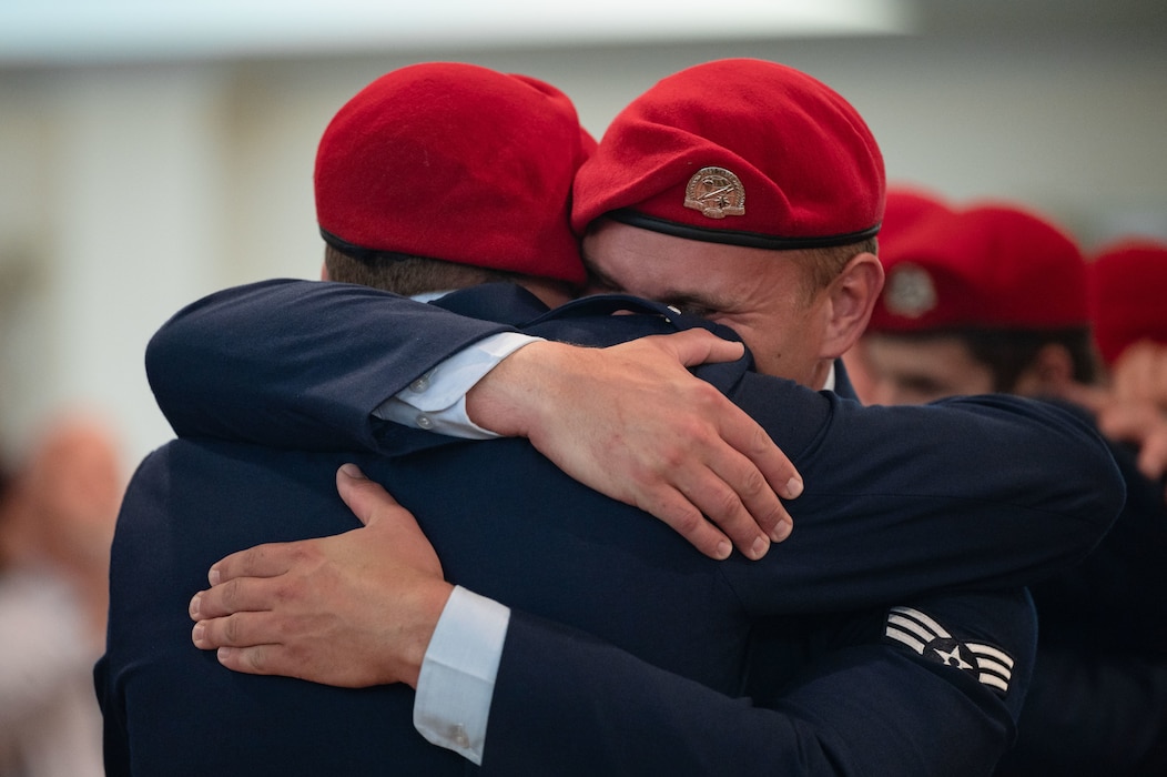 two Airmen wearing new, bright red berets embrace