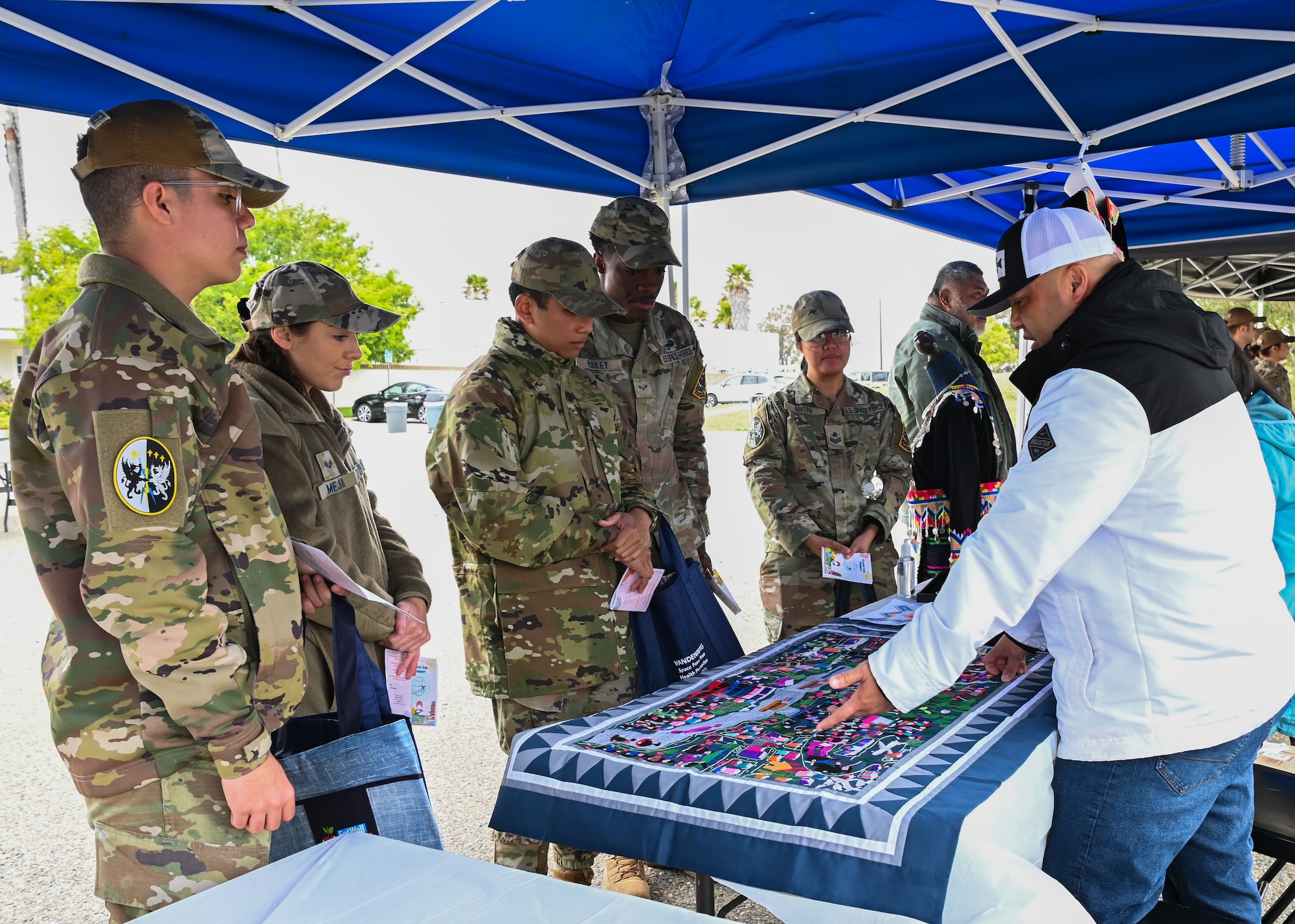 Master Sgt. Jessie Lee, 30th Healthcare Operations Squadron senior enlisted leader, explains the history displayed of the Hmong people on the tapestry placed on the table during the Around the World passport event at Vandenberg Space Force Base, Calif., May 19, 2023. The Hmong people are an indigenous group in East and Southeast Asia. (U.S. Space Force photo by Senior Airman Tiarra Sibley)