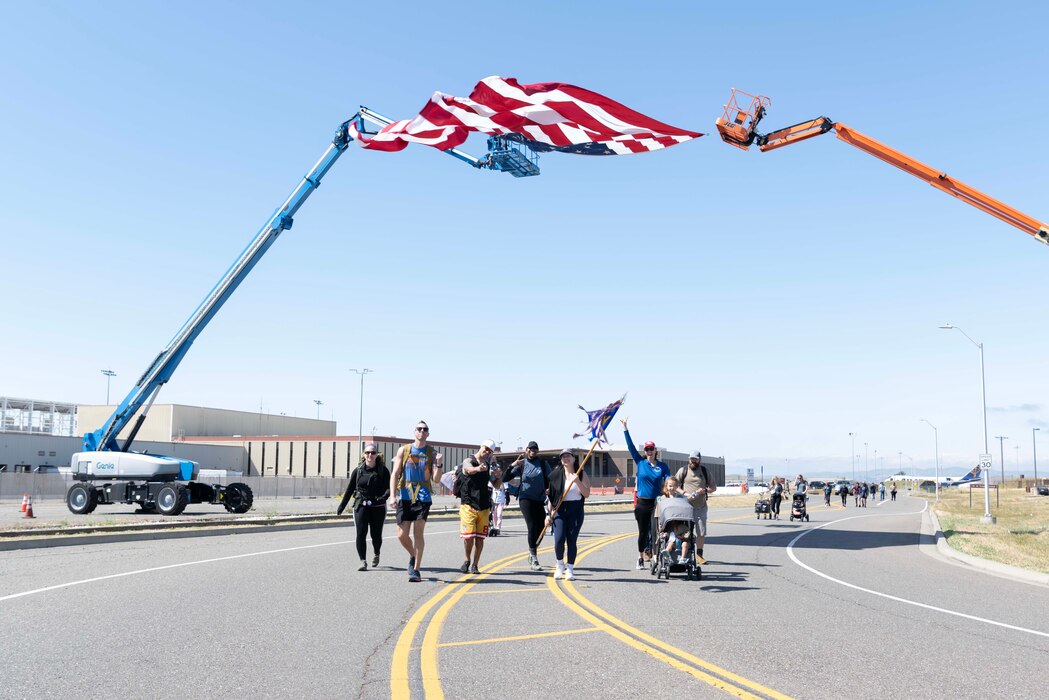 Airmen and their families walk under a large American flag.