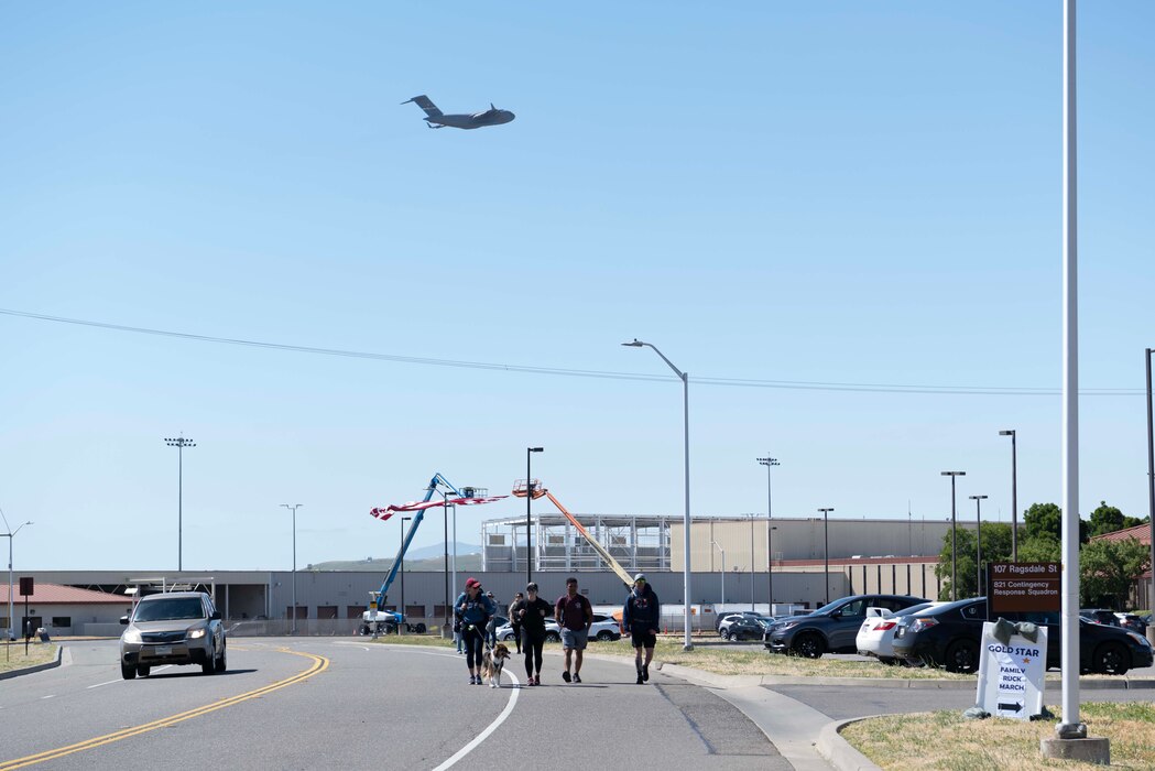 Airmen and their families walk down a road with a large military aircraft in the background.