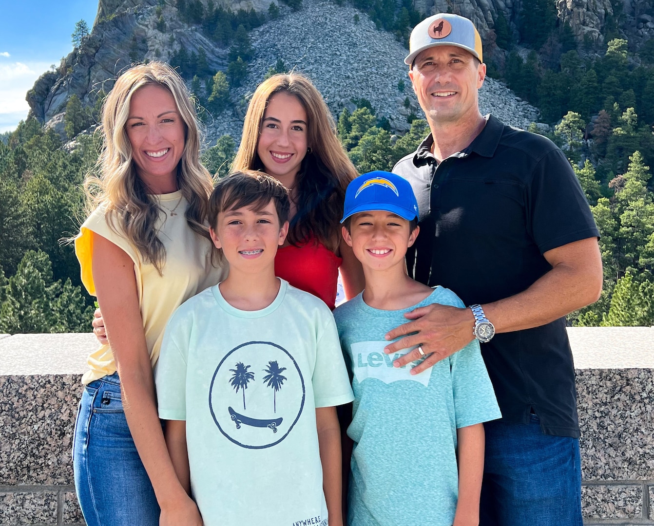 A family of five poses in front of a hillside.