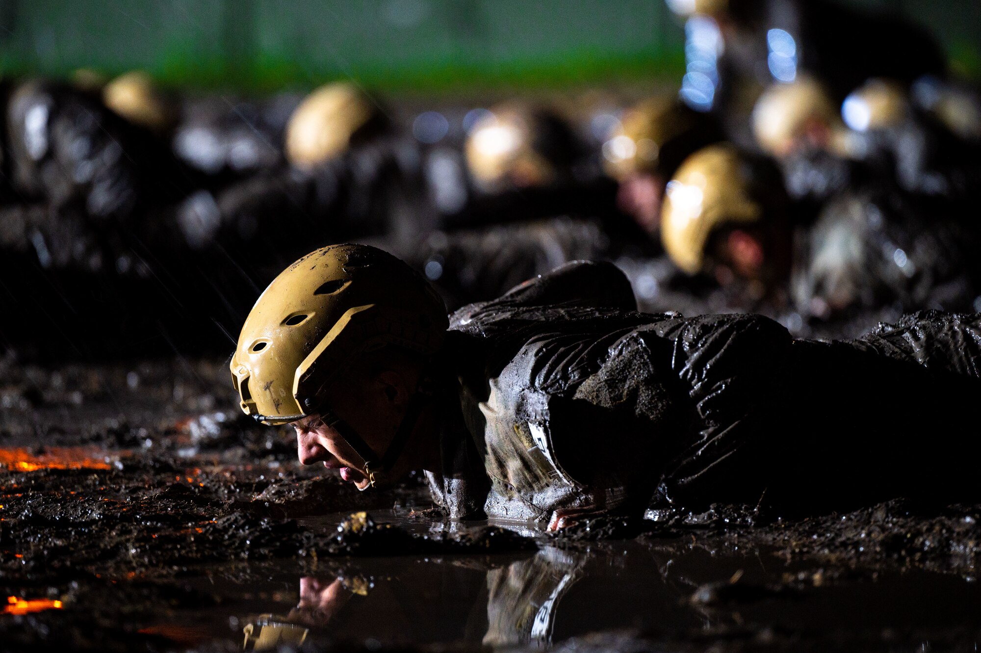 Trainees in bright yellow helmets complete pushups in the mud while it rains