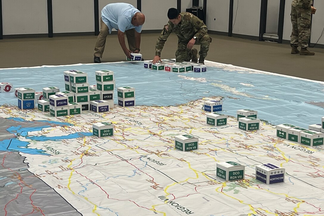 Two men place small boxes on a large map.