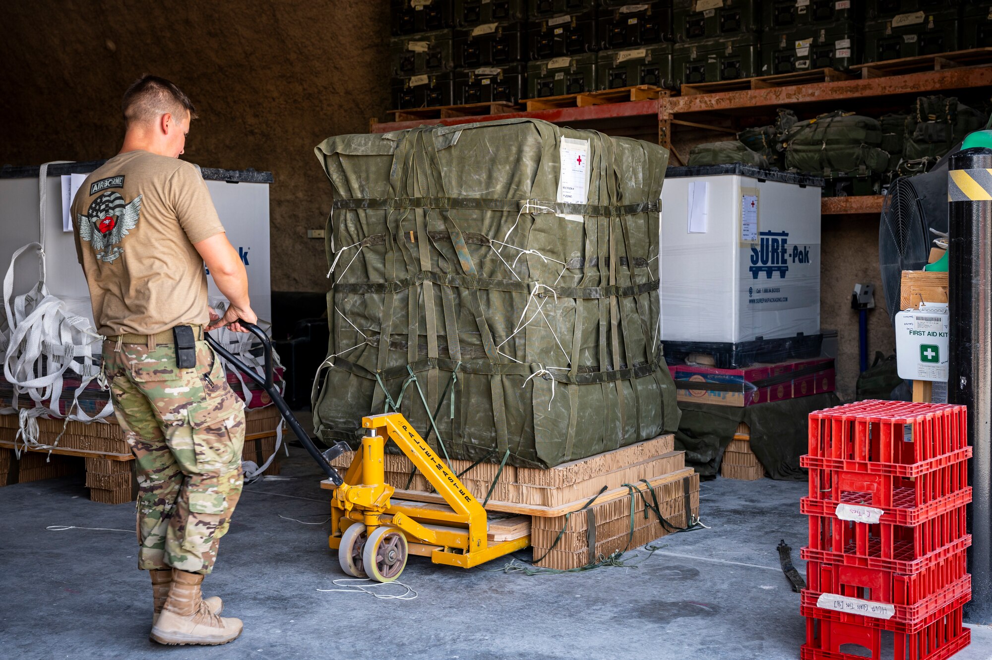 A military member lifts a supply crate with a dolly