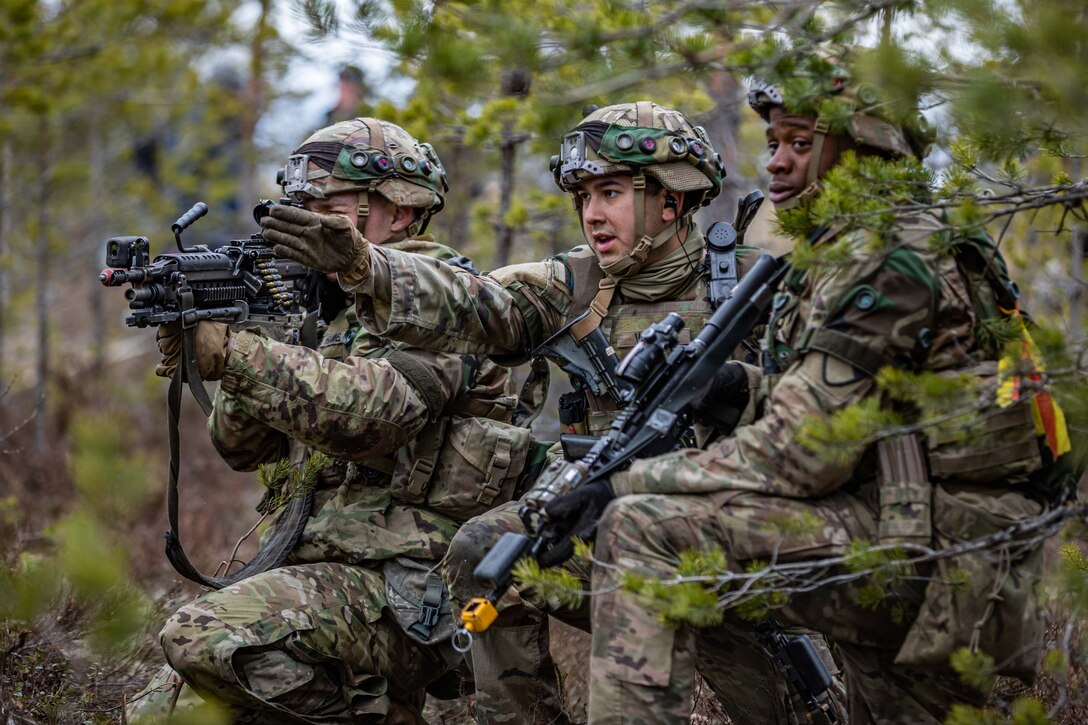 A soldier in the center motions to move forward while two other soldiers on both sides holding weapons look on.