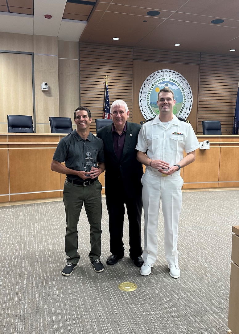 Lt. j.g. Paul Strunc, left, a critical care nurse at Naval Medical Center Portsmouth, Virginia Beach Mayor Bobby Dyer, center, and Tyler Volpe pose for a photo after they were both presented the Virginia Beach Mayor’s Lifesaving Award at City Hall, May 8.Strunc was recognized for administering lifesaving cardiopulmonary resuscitation on a civilian at the beach on Oct. 2, 2022. Through their rapid intervention and emergency response, the person was stabilized until ambulatory services arrived on the scene. (U.S. Navy photo by Lt. Nube Macancela)
