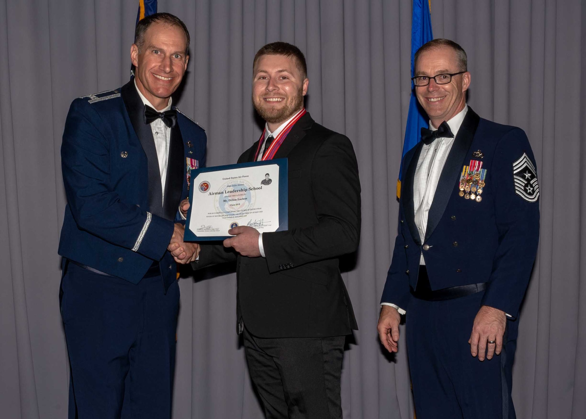 Dillon Lackus, center, Air Force Mortuary Affairs Operations mortuary clerk, is presented a graduation certificate by Col. Matt Husemann, left, 436th Airlift Wing commander, and Chief Master Sgt. Timothy Bayes, right, 436th AW command chief, during the Staff Sgt. Julio Alonso Airman Leadership School, Class 23-E, graduation ceremony at The Landings on Dover Air Force Base, Delaware, May 18, 2023. Lackus was the first civilian Airman to graduate from the five-week course that prepares military and civilian Airmen for leadership roles in the Air Force. (U.S. Air Force photo by Staff Sgt. Faith Barron)