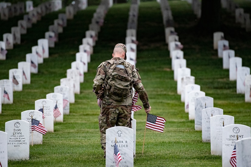A soldier places flags on headstones.