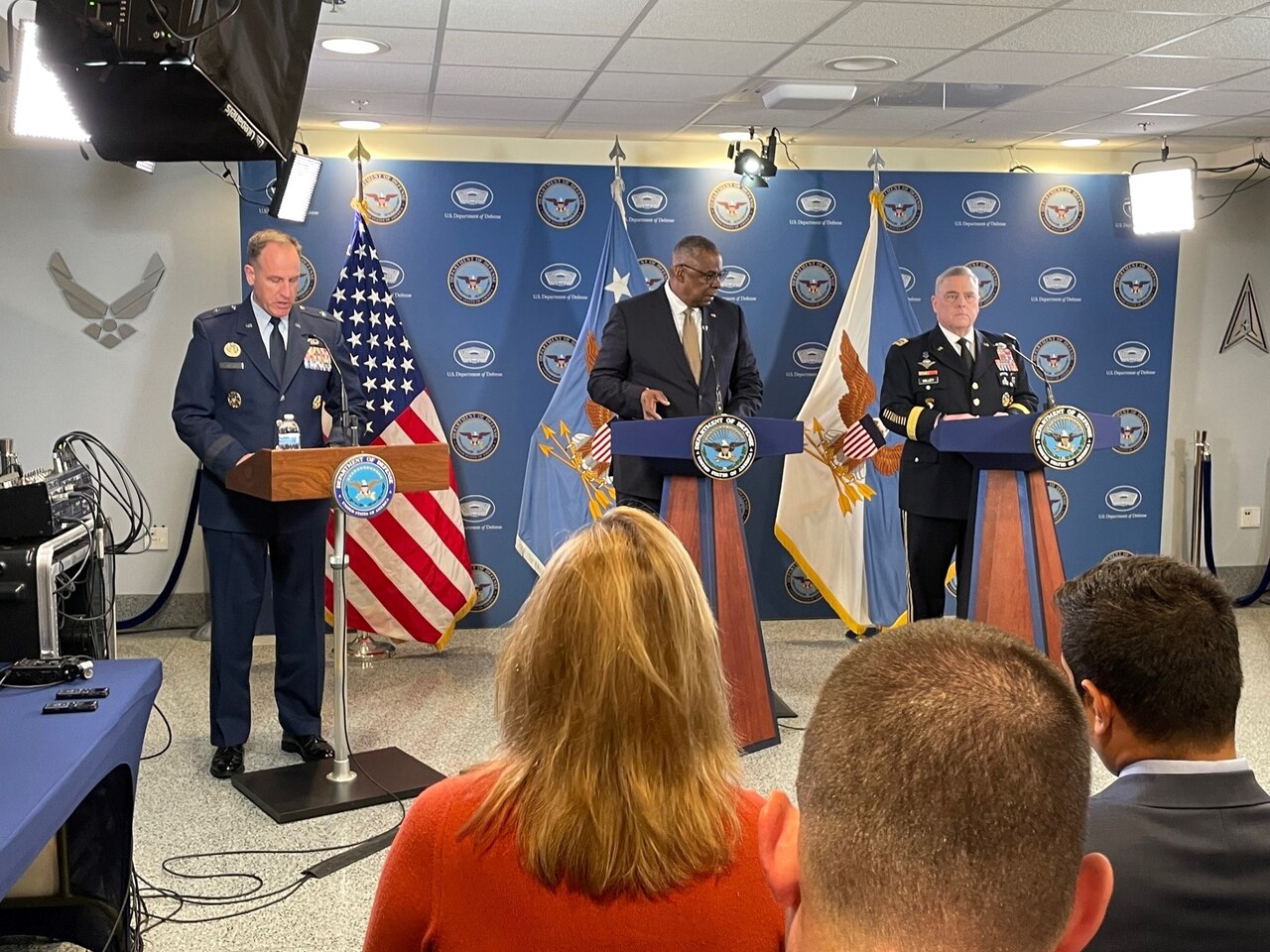 Three men stand behind lecterns at news conference.