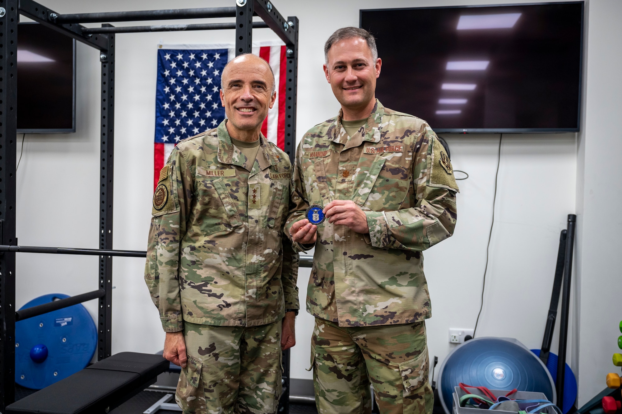 Two military members pose for a photo displaying a coin.