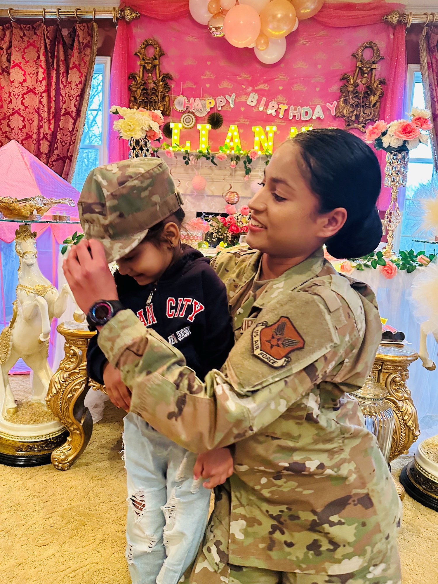 Woman in military uniform kneeling down with a child while putting her hat on the child