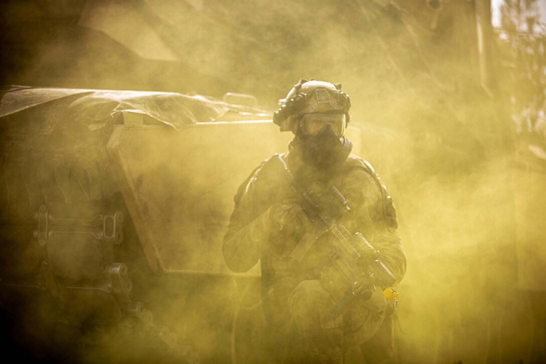 A soldier stands in the middle of green fog in full military gear and mask.