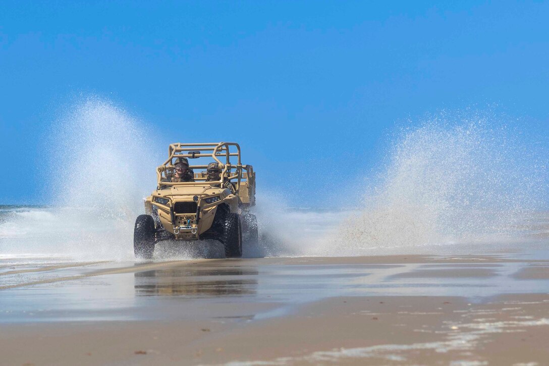 Marines ride in a military vehicle through a puddle of water.