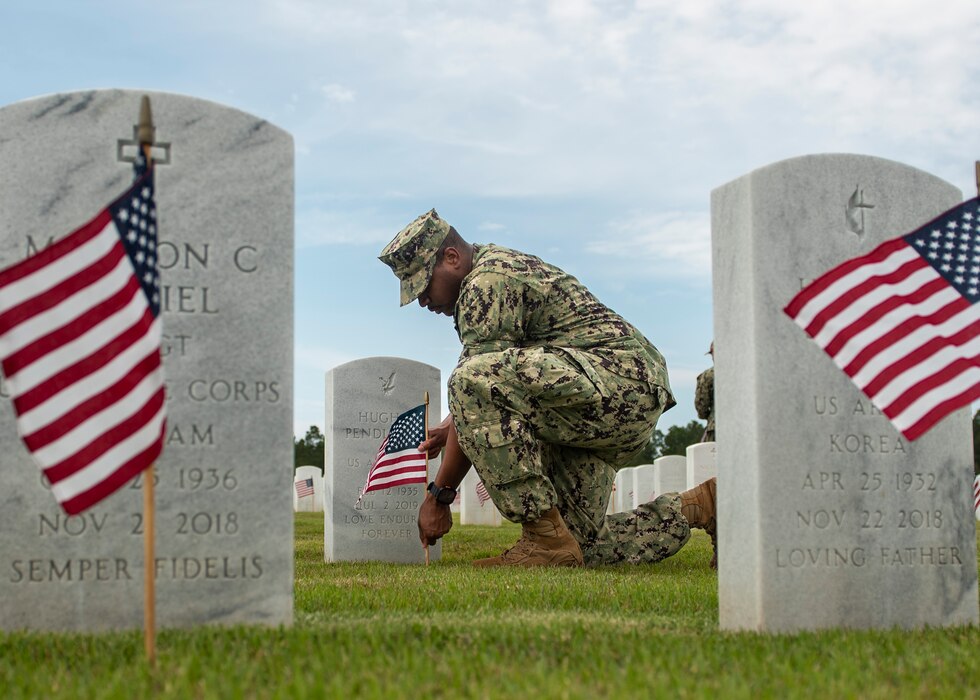 Religious Programs Specialist 2nd Class Justin Knight places a flag on a grave at the Jacksonville National Cemetery in preparation for Memorial Day.