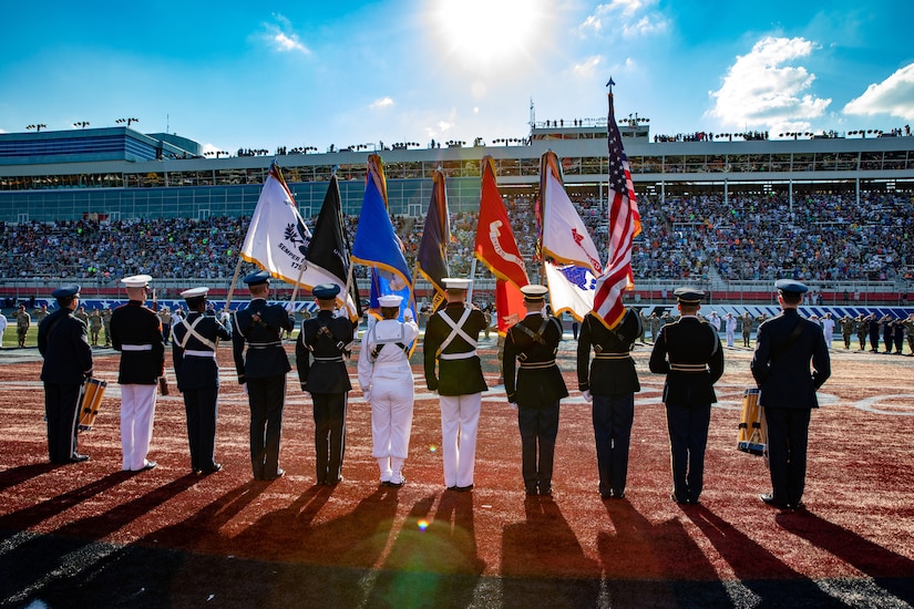A color guard stands facing a grandstand filled with people.