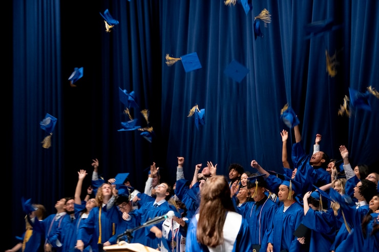 a crowd of students in graduation gowns toss their caps in the air
