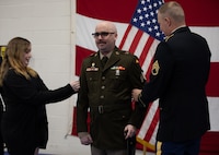 Staff Sgt. Tom Roy and Rebecca Raygoza wife of newly-promoted Sgt. Maxwell Ehrlich pins the rank of sergeant on him during his promotional ceremony May 6, 2023 at North Riverside Armory, Chicago Illinois. Ehrlich, assigned to Charlie Battery, 2-218th Field Artillery Battalion based in Portland Oregon, gets promoted as result of his hard work and dedication in the Army National Guard.