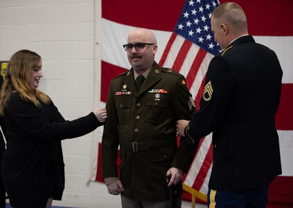 Staff Sgt. Tom Roy and Rebecca Raygoza wife of newly-promoted Sgt. Maxwell Ehrlich pins the rank of sergeant on him during his promotional ceremony May 6, 2023 at North Riverside Armory, Chicago Illinois. Ehrlich, assigned to Charlie Battery, 2-218th Field Artillery Battalion based in Portland Oregon, gets promoted as result of his hard work and dedication in the Army National Guard.