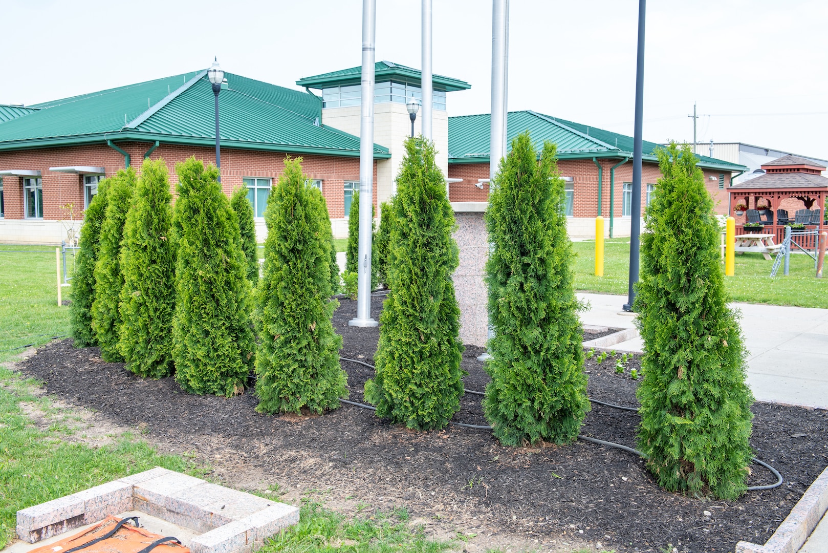 A photo of green triangle shaped evergreen trees behind a grouping of flagpoles and a stone monument.
