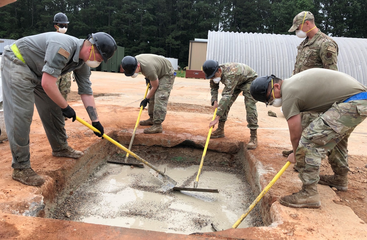 Airmen smooth the surface of concrete in a large hole.